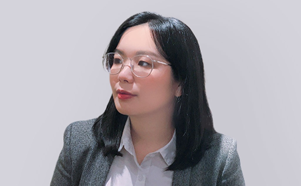 Cindy Yeh is wearing a suit jacket and has shoulder length black hair and glasses and is front of a neutral background.