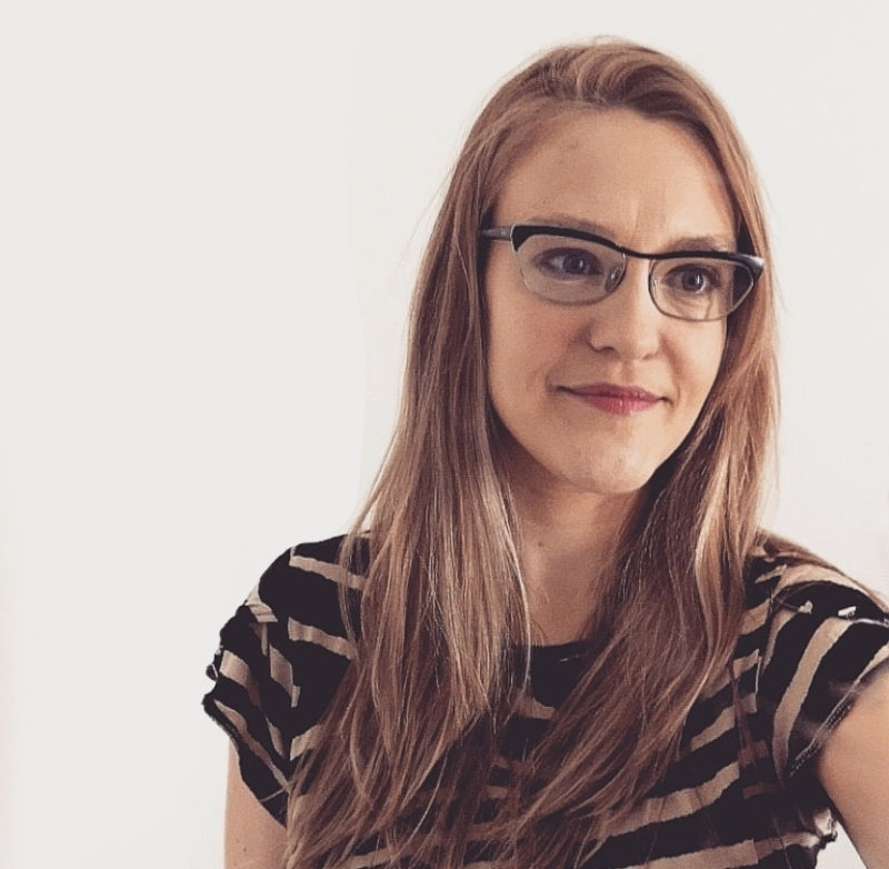 Beth Granter has long blond hair, funky retro glasses and a stripey t-shirt. She is shown to one side of the frame in front of a neutral background.