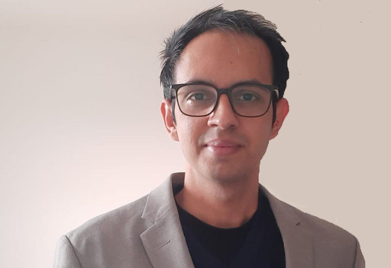 Himanshu Mewada is has short cropped hair and is wearing black rimmed glasses. He is wearing a light coloured blazer and a black t-shirt.