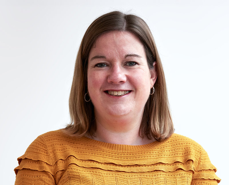 Sharon Webster is has shoulder length brown hair and is wearing a mustard coloured knitted jumper with design flourishes.