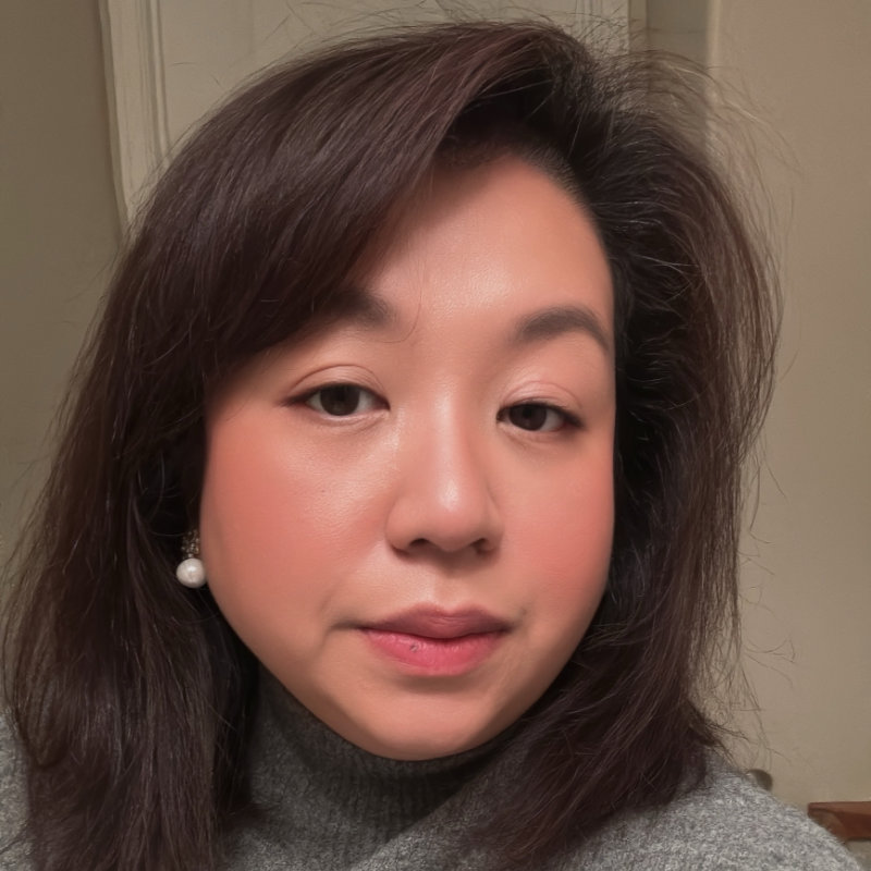 Zaianne Sparrow has shoulder length brown hair and is wearing a grey polo neck sweater. She is wearing pearl earrings.