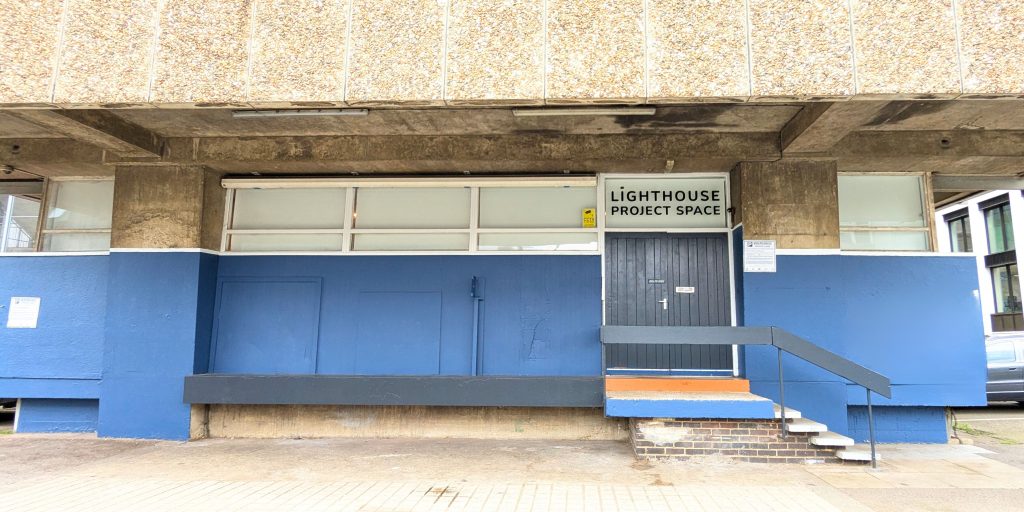 The back of New England House is shown. It is painted with a blue stripe and the labelled door for the Lighthouse project space is shown.