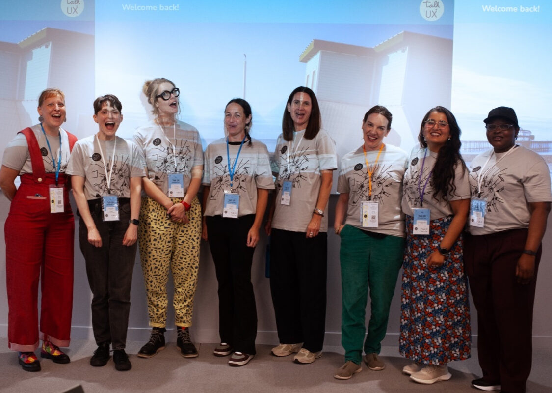 The Talk UX organisers stand in a row in front of a projection screen on the first day.